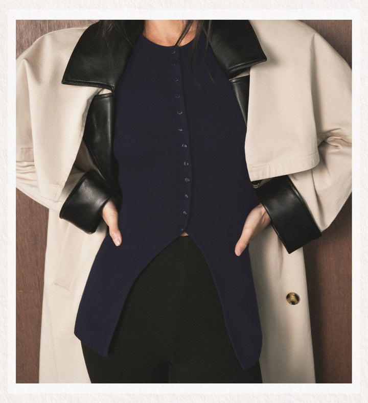 Person wearing a navy blue dress with a beige coat and black leather sleeves.