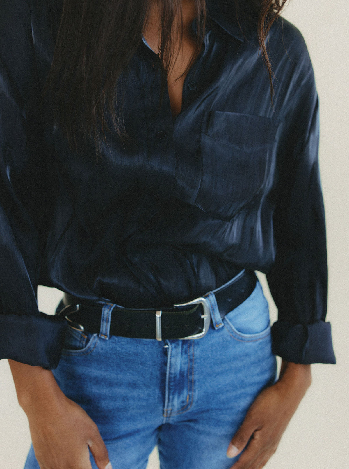 A person wearing a sheer black organza long-sleeve button-up shirt tucked into blue jeans with a black belt, shown from the chest down against a plain light background.